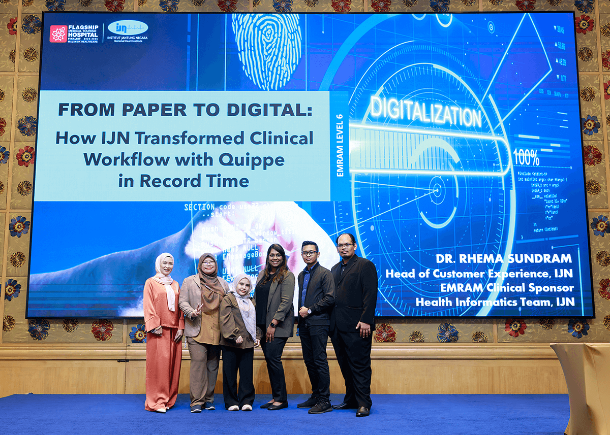 Representatives from Institut Jantung Negara (IJN) in Malaysia stand in front of a presentation titled 'From Paper to Digital: How IJN Transformed Clinical Workflow with Quippe in Record Time' at the 2025 Medicomp U in Bangkok, Thailand.